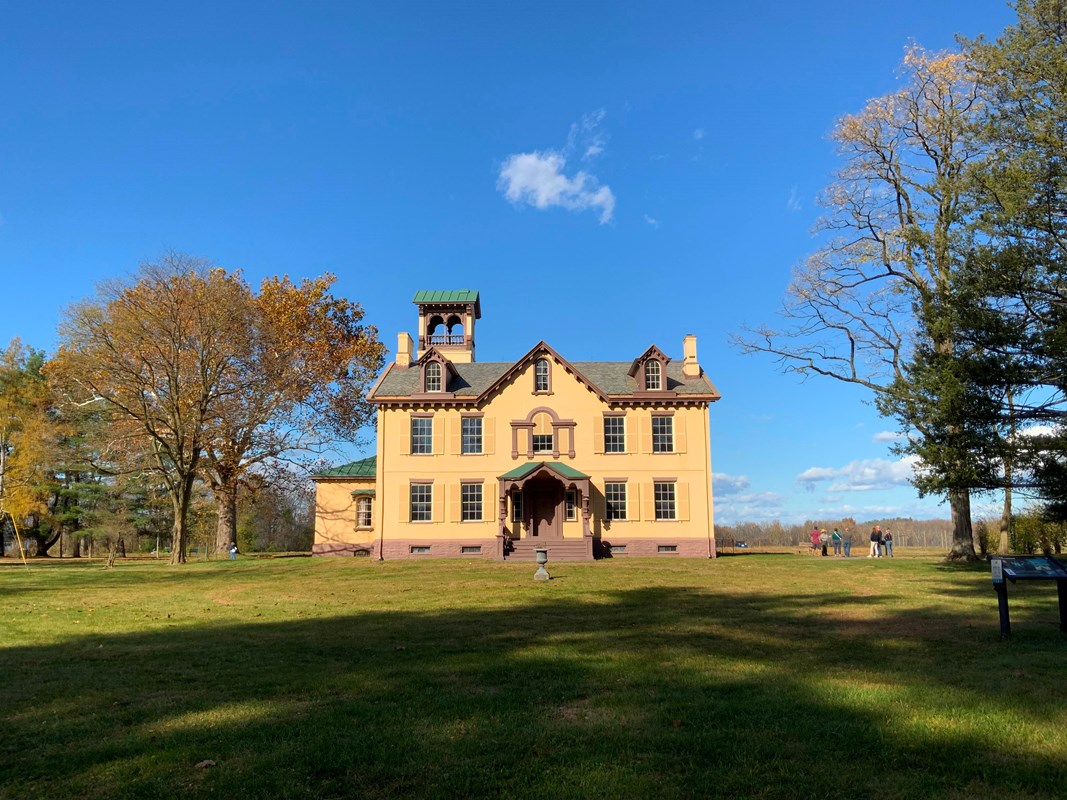 Lindenwald, a yellow, 3 story mansion, is surrounded by trees. 