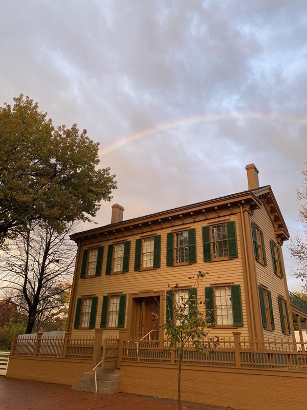 The two-story, tan Lincoln Home with a rainbow in the sky above it.