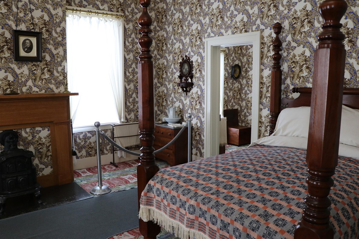A bedroom with a patterned carpet and wallpaper, a large four poster bed, and a fireplace.