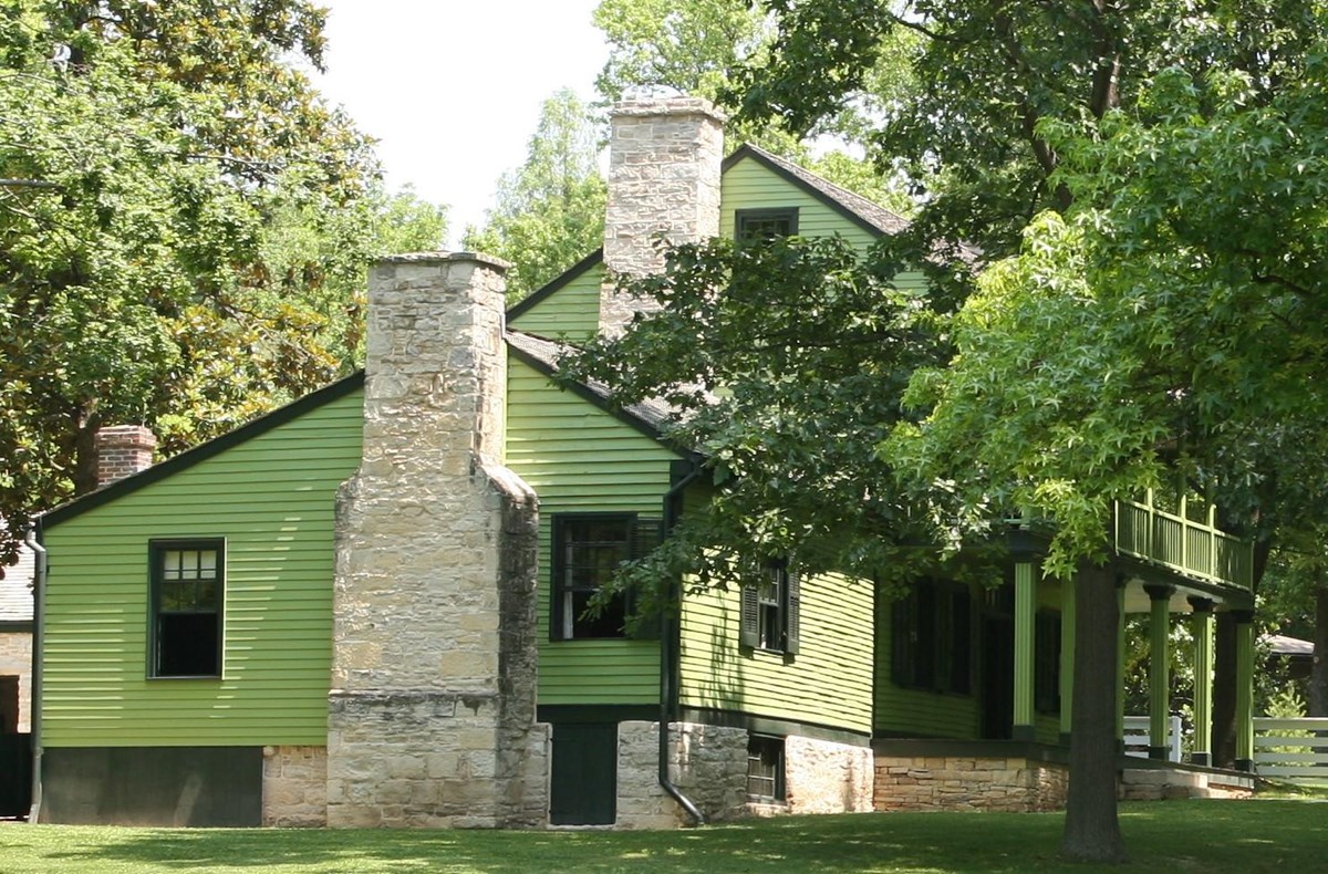 Green sided, two story house with green trees