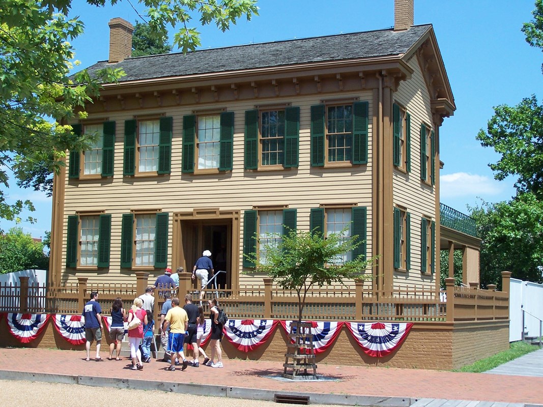 A guide leading a group into the Lincoln Home which has bunting on the front.