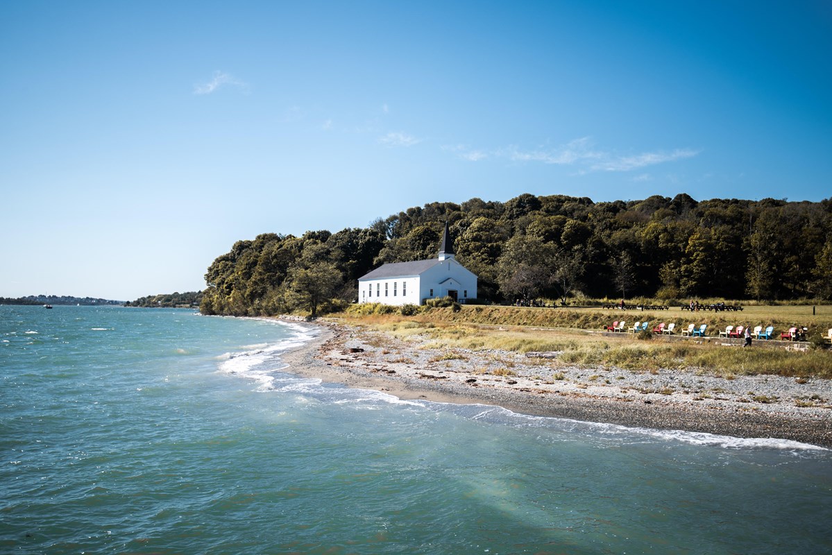 Beach on Peddocks Island, with a white chapel and forested area in the background.