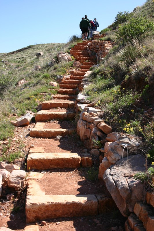 A handful of hikers at the top of a grassy hill with a long set of red stone steps