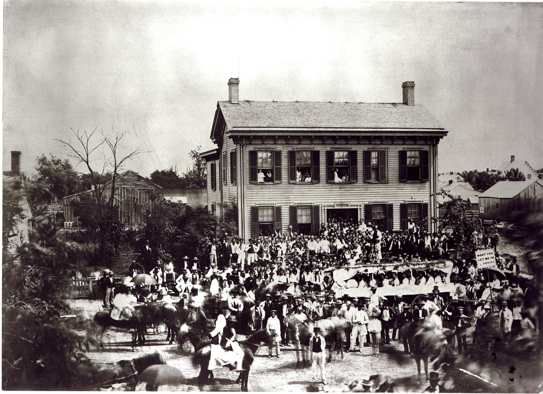 A black and white image of a crowd of people standing in front of and around the Lincoln Home.