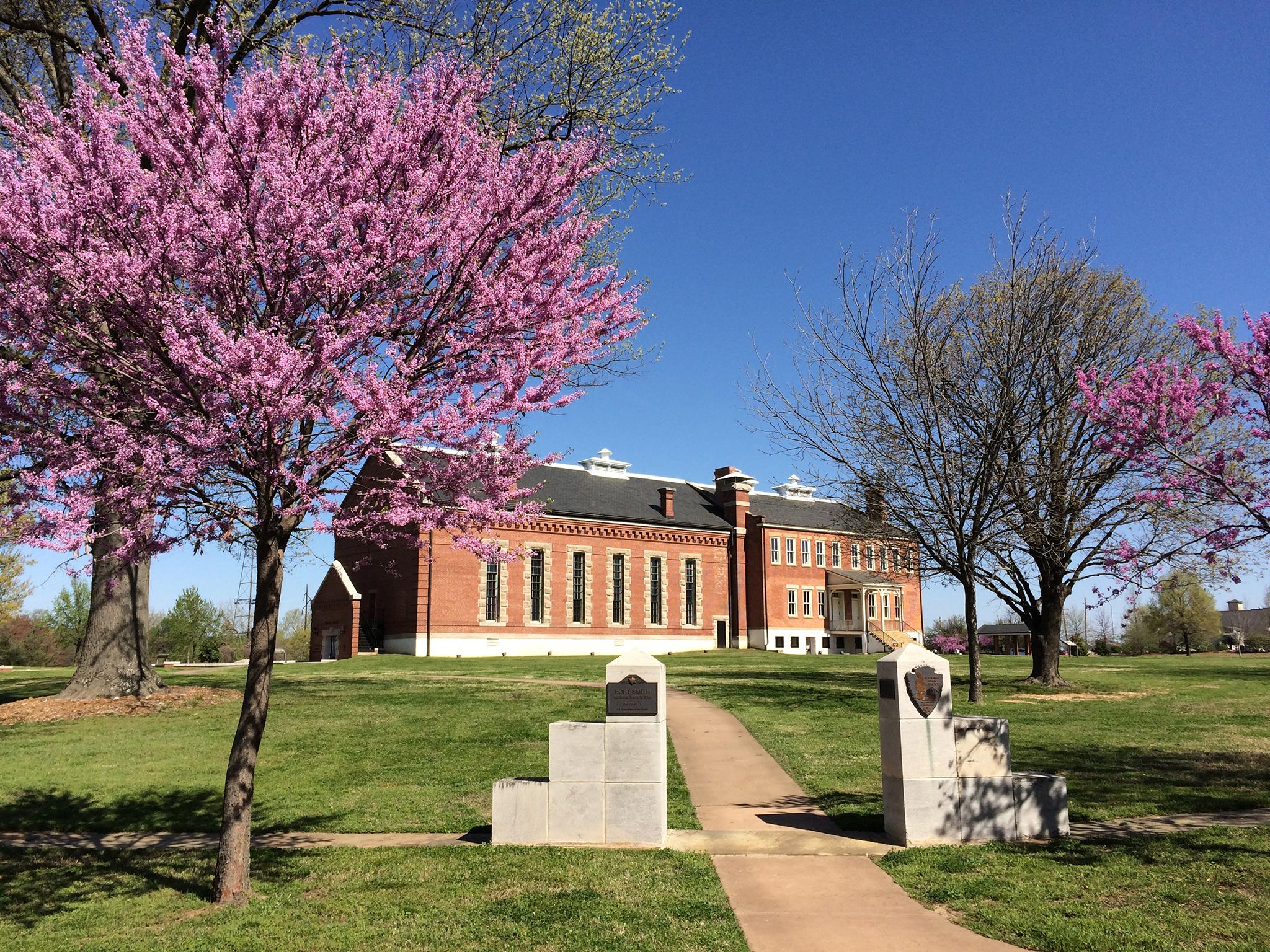 The red brick visitor center framed by two redbud trees with a paved path leading to it.