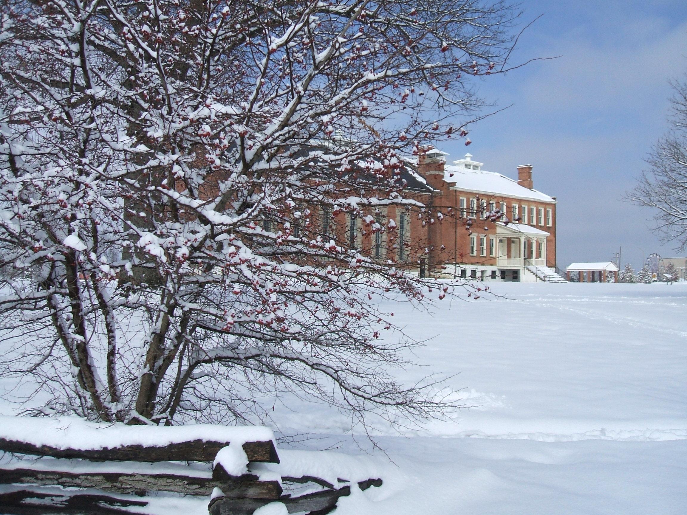 A snow-covered Hawthorn bush partially obscures the red brick visitor center in the background.