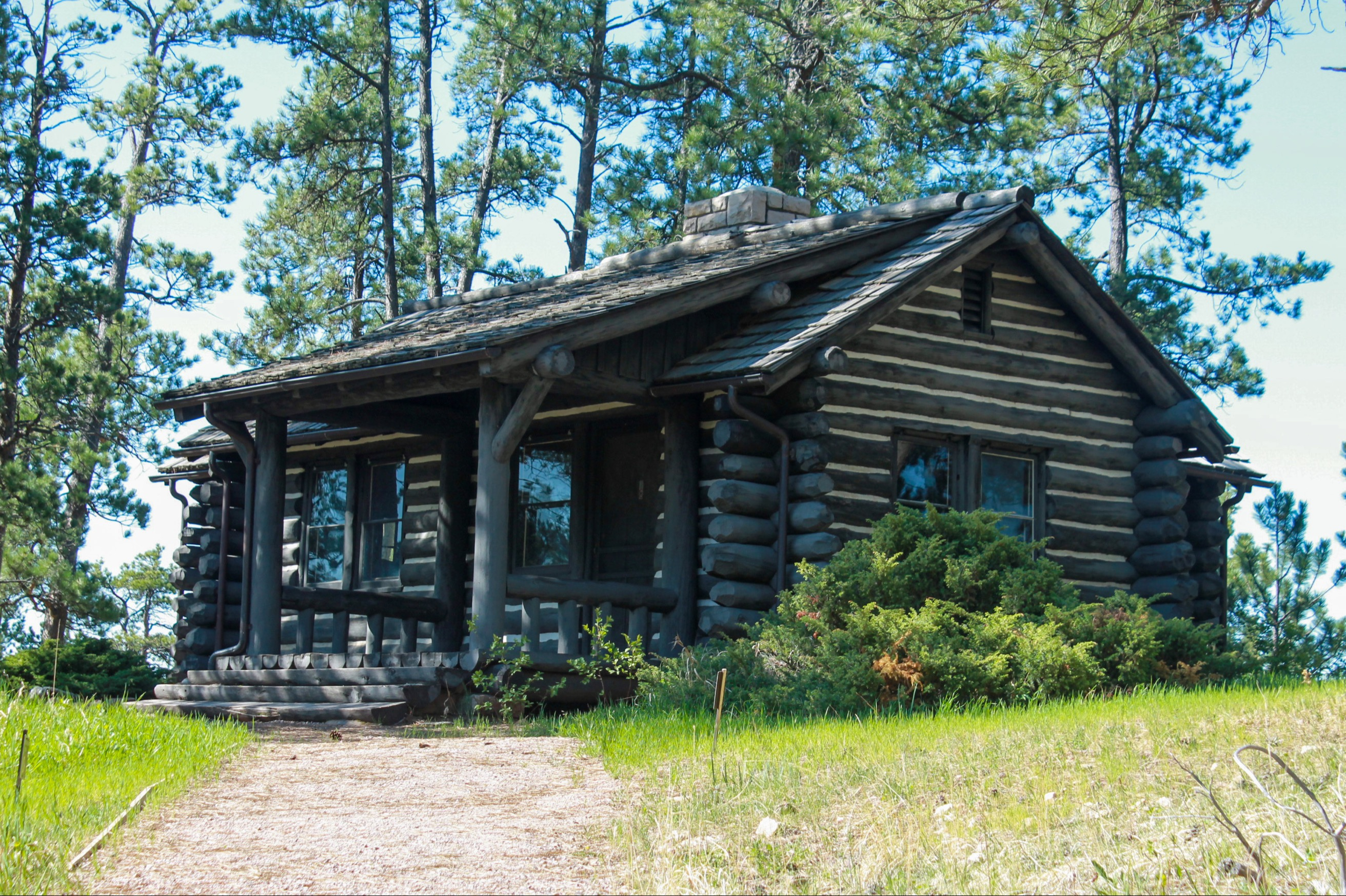 A small, dark-brown cabin sits on top of a hill with a walking path leading to its front porch.