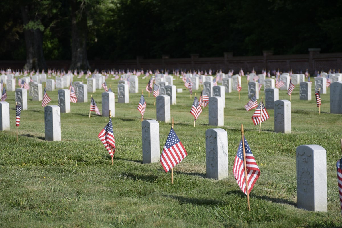 Small American flags flutter in front of white marble headstones. 