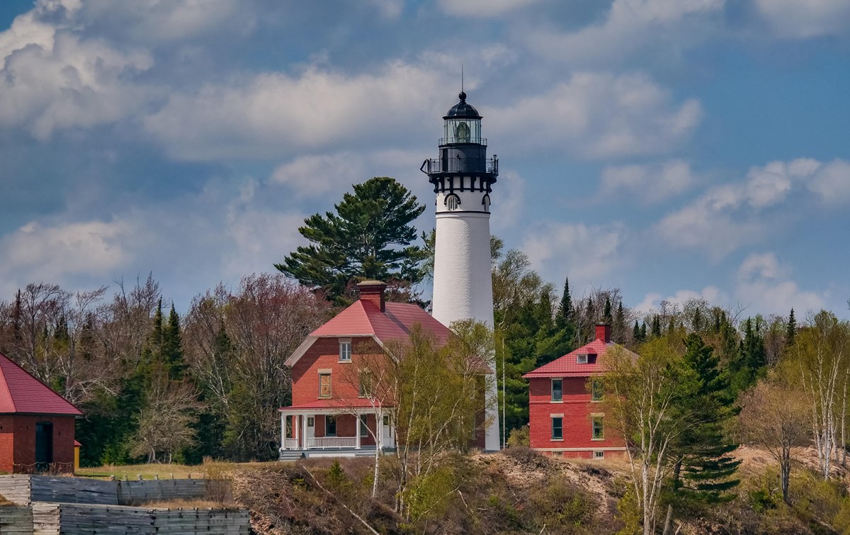 A white lighthouse tower surrounded by red brick buildings on a sunny day. 