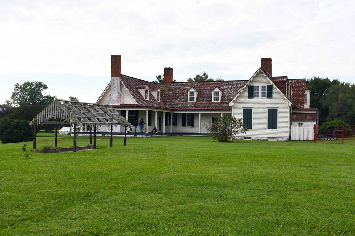 An arbor stands 20 feet in front of a two story white house with a red shingled roof.