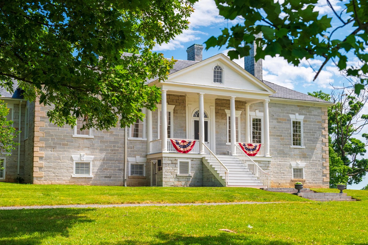 American flag bunting hangs from the porch on a limestone building with a white portico.
