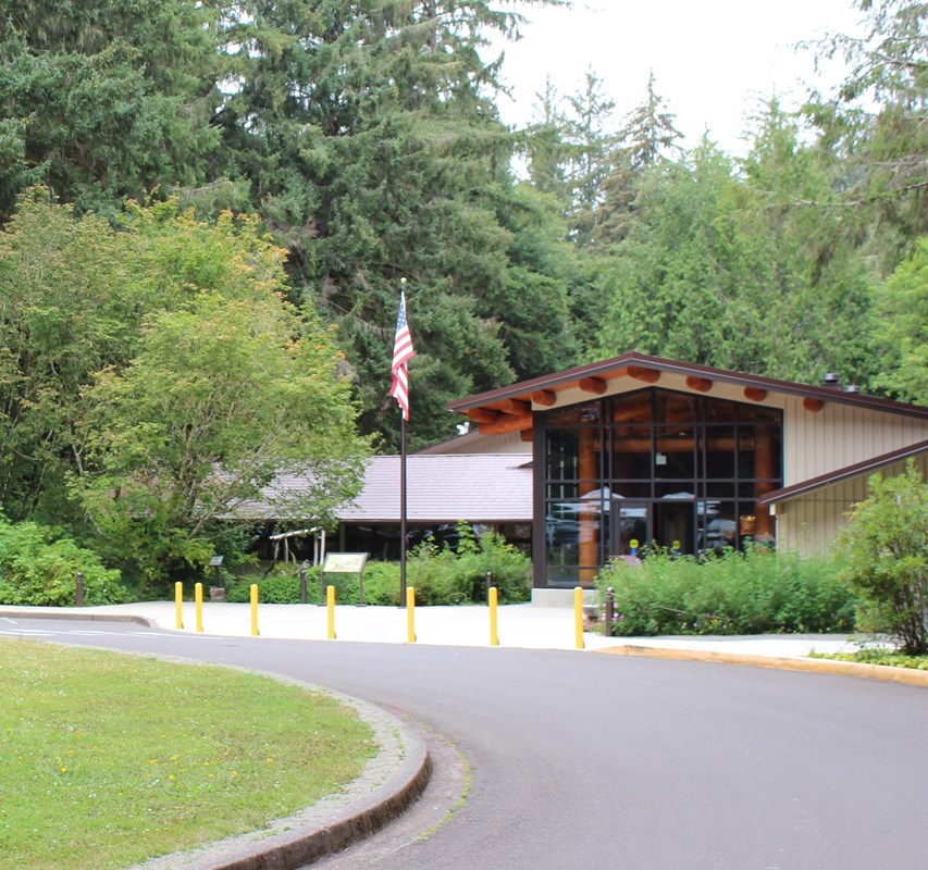 The Fort Clatsop Visitor Center, the front covered in large windows and large trees surrounding it.