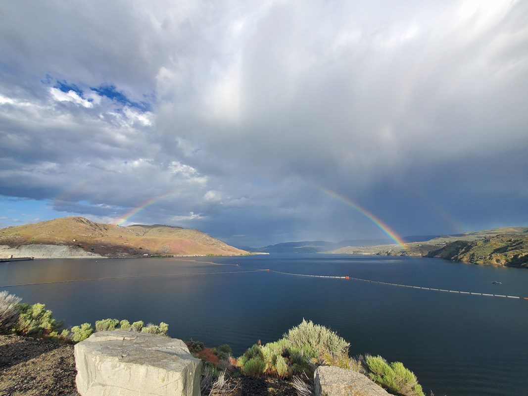 Stormy clouds over a blue lake with a rainbow stretching from one side of the lake to the other.