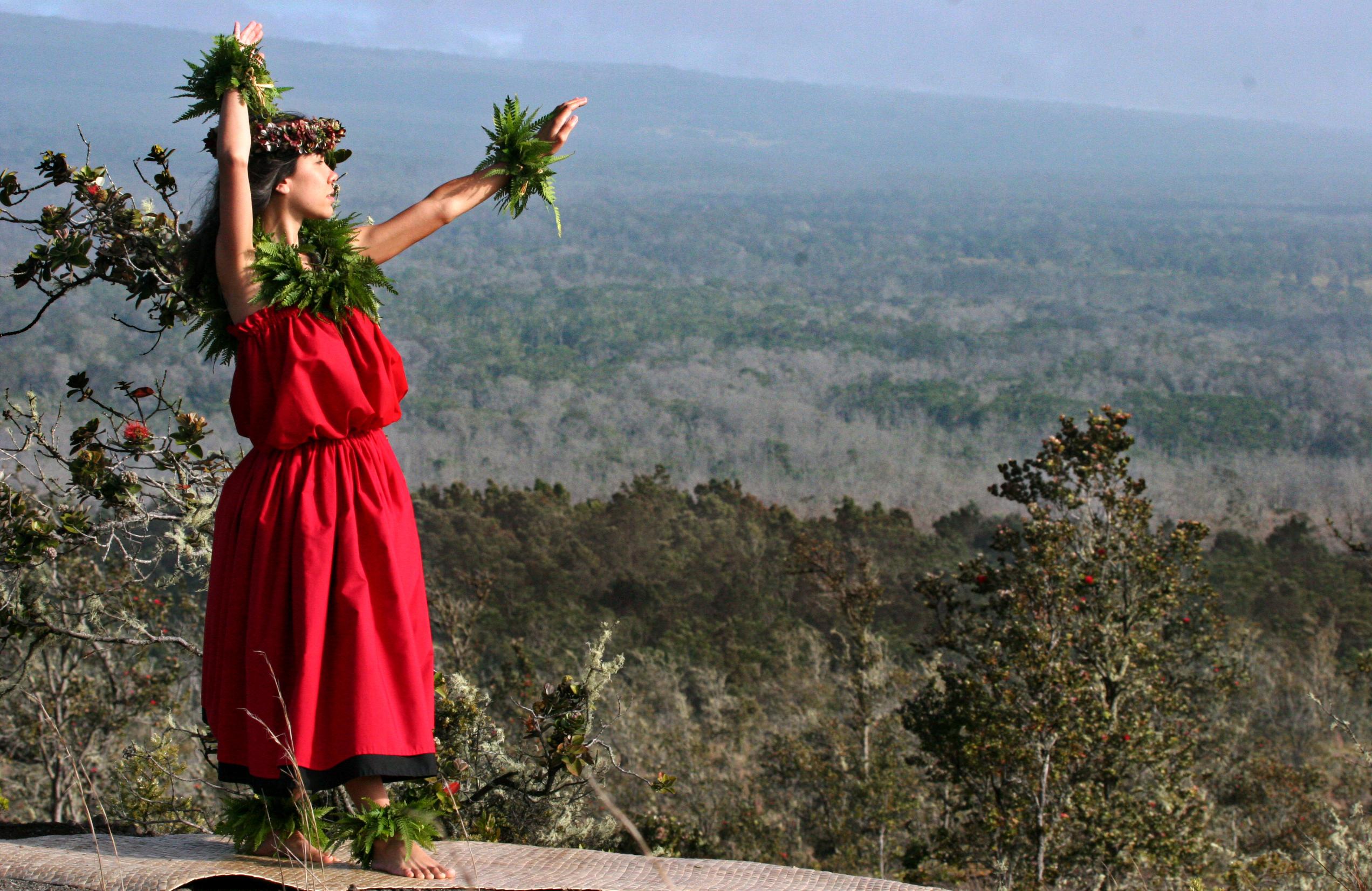 A hula dancer in a red dress above a forested area