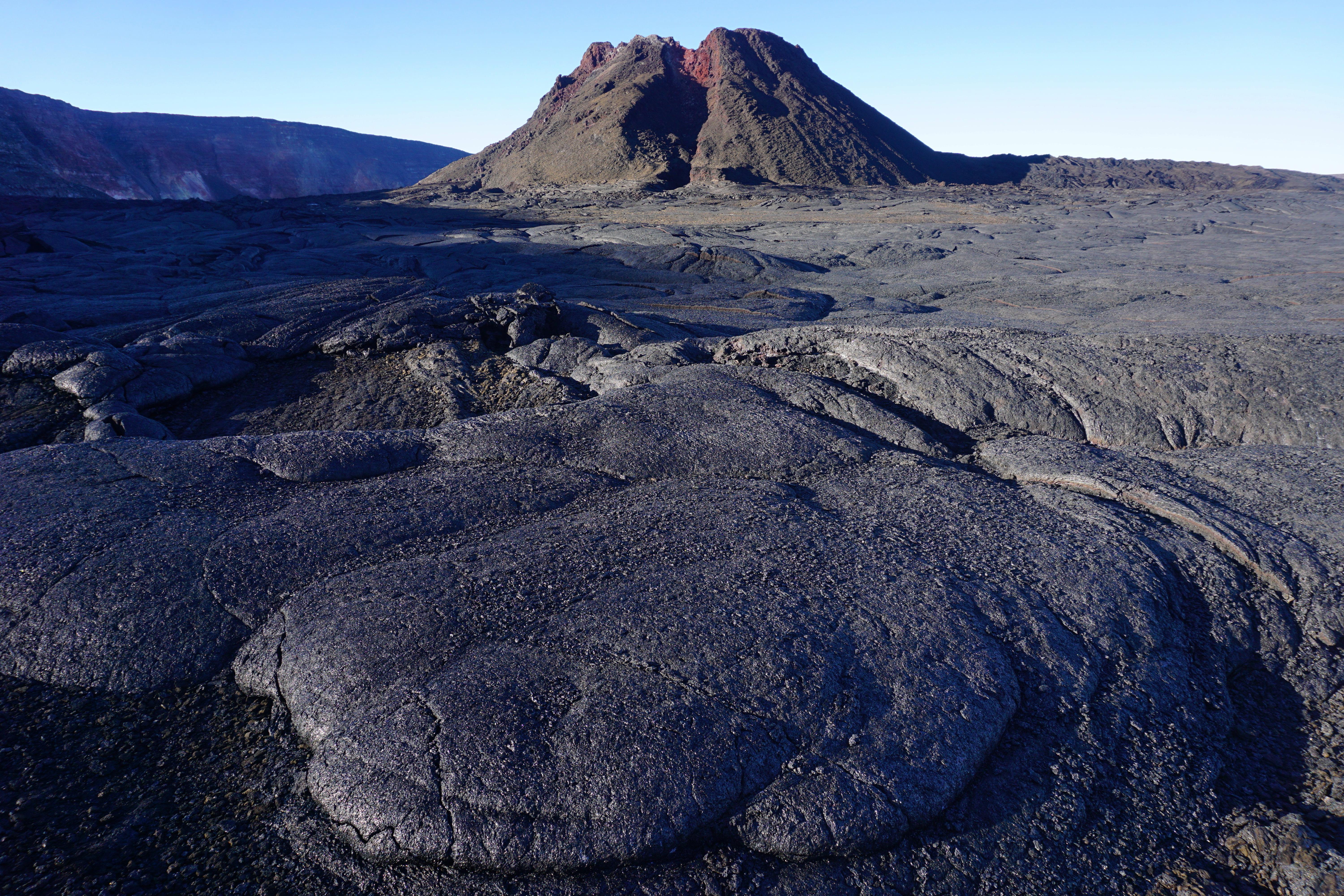 A lava cone rising behind a flow of lava with caldera walls beyond