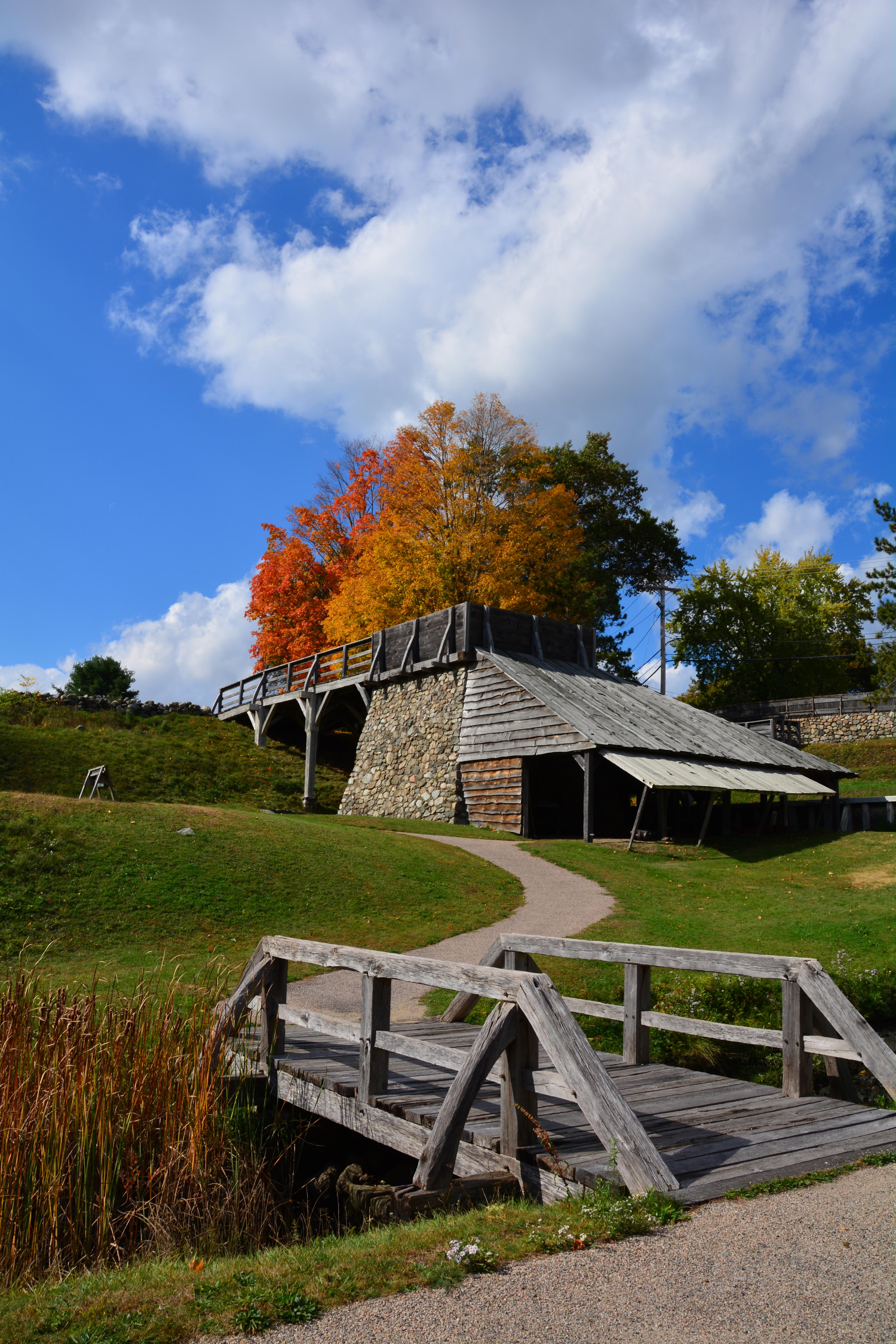 Rectangular wooden structure between orange deciduous trees and wooden bridge with walkway.