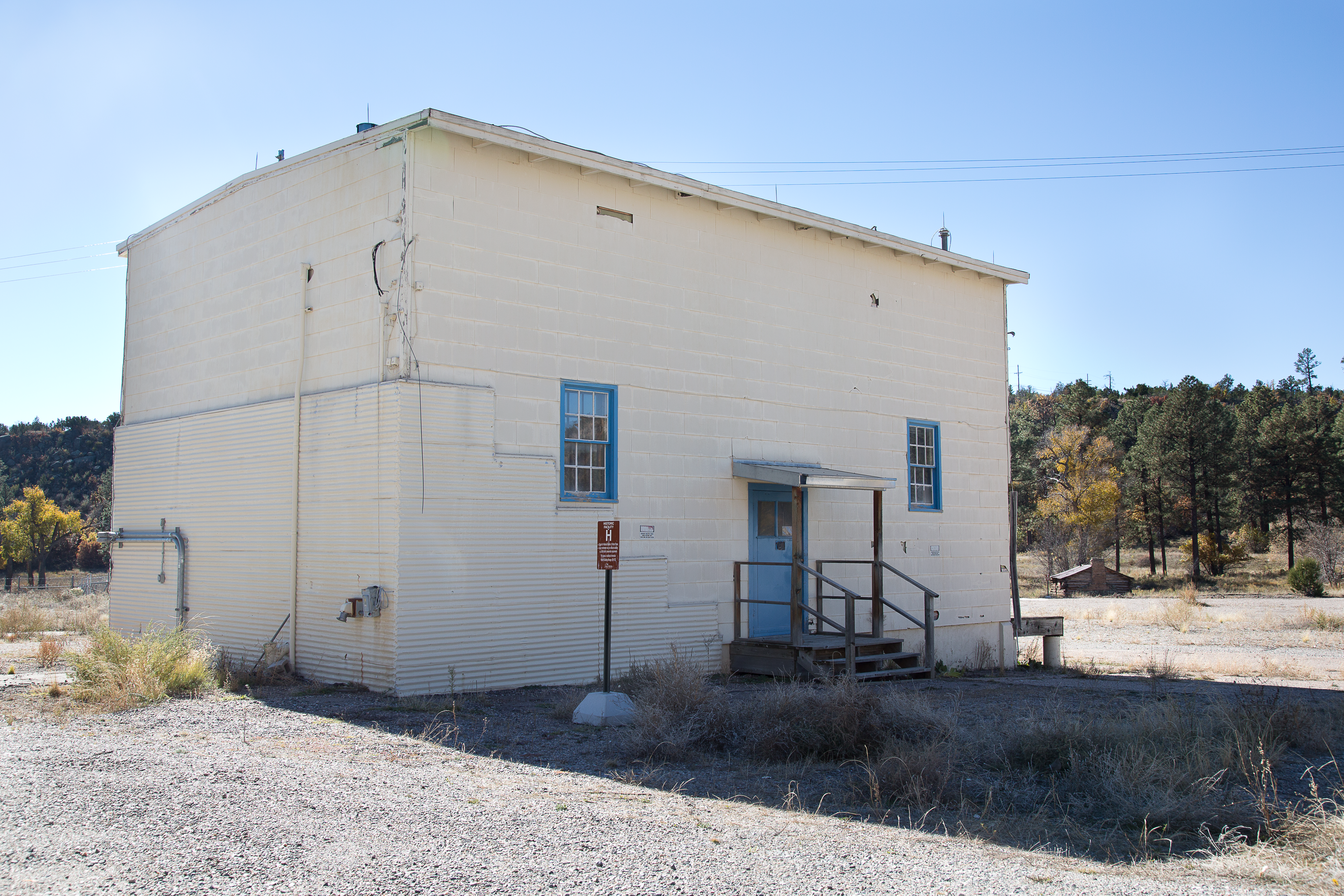 Two-story white house with two small windows, a single door, and flat roof stands in a gravel lot.