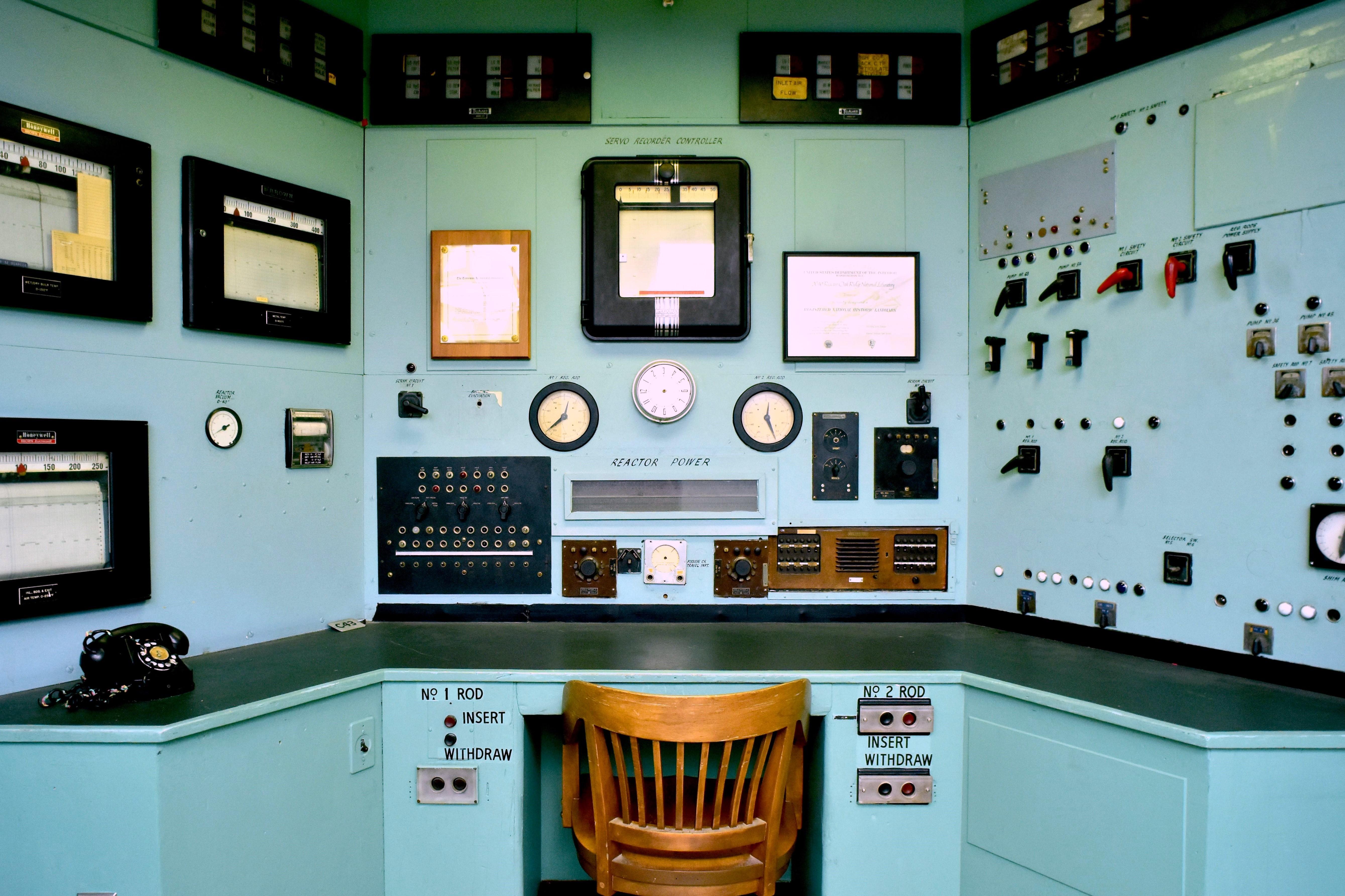 Wooden chair sits amid light blue paneling covered in dials, meters, screens, and buttons.