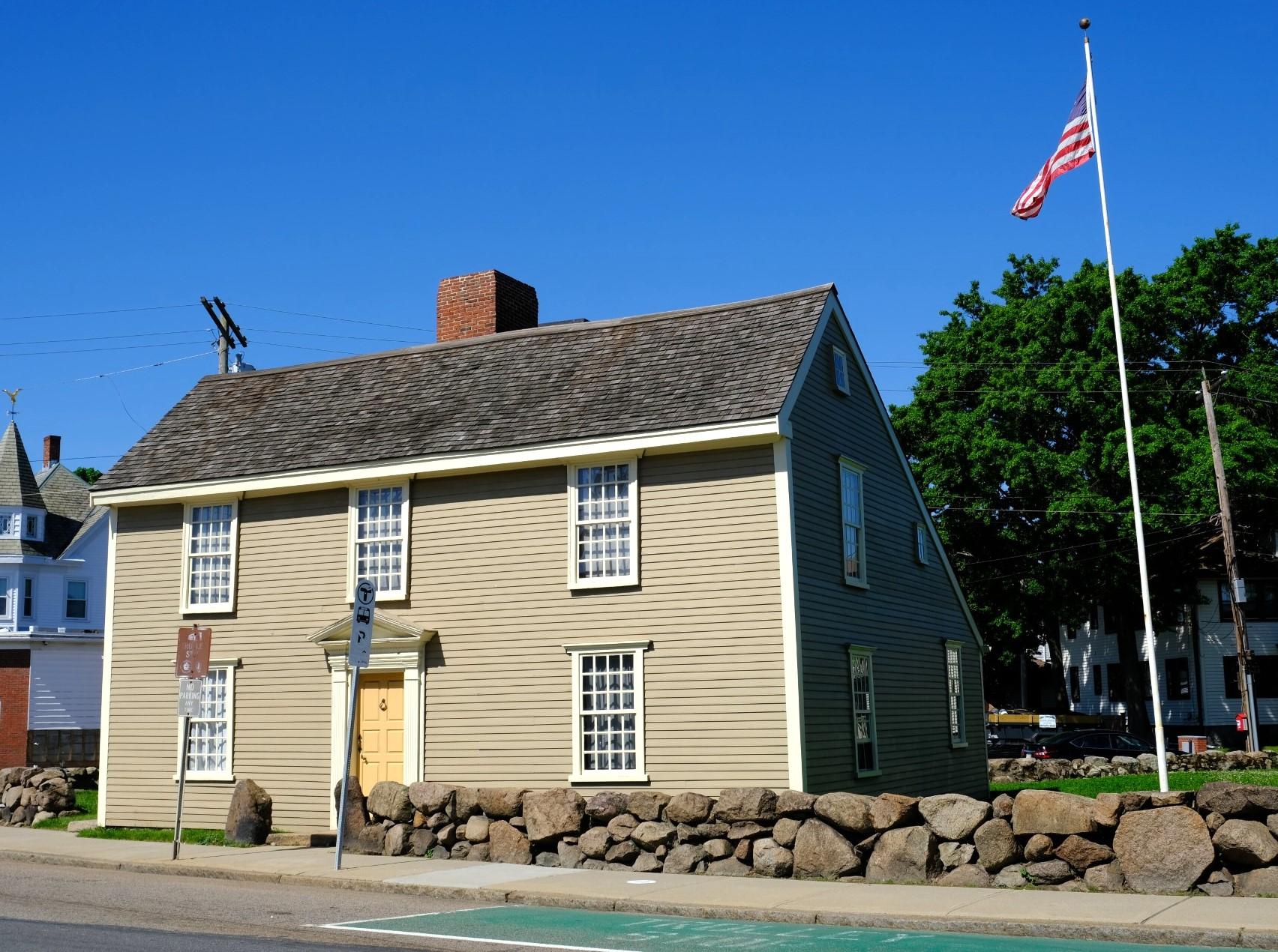 A New England "salt-box" style house with light gray siding and a beige door.