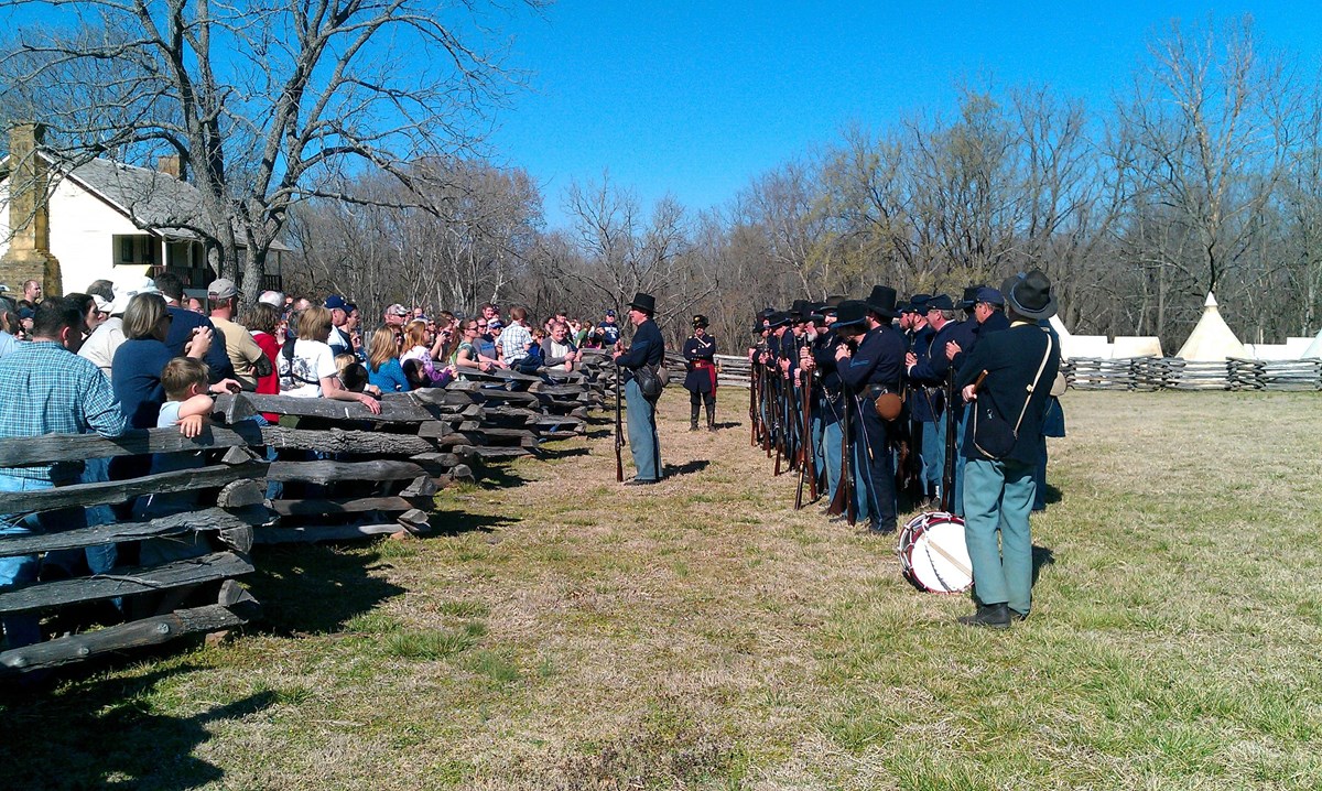 Photo of Union Infantrymen reenactors standing in front of building with large crowd. 
