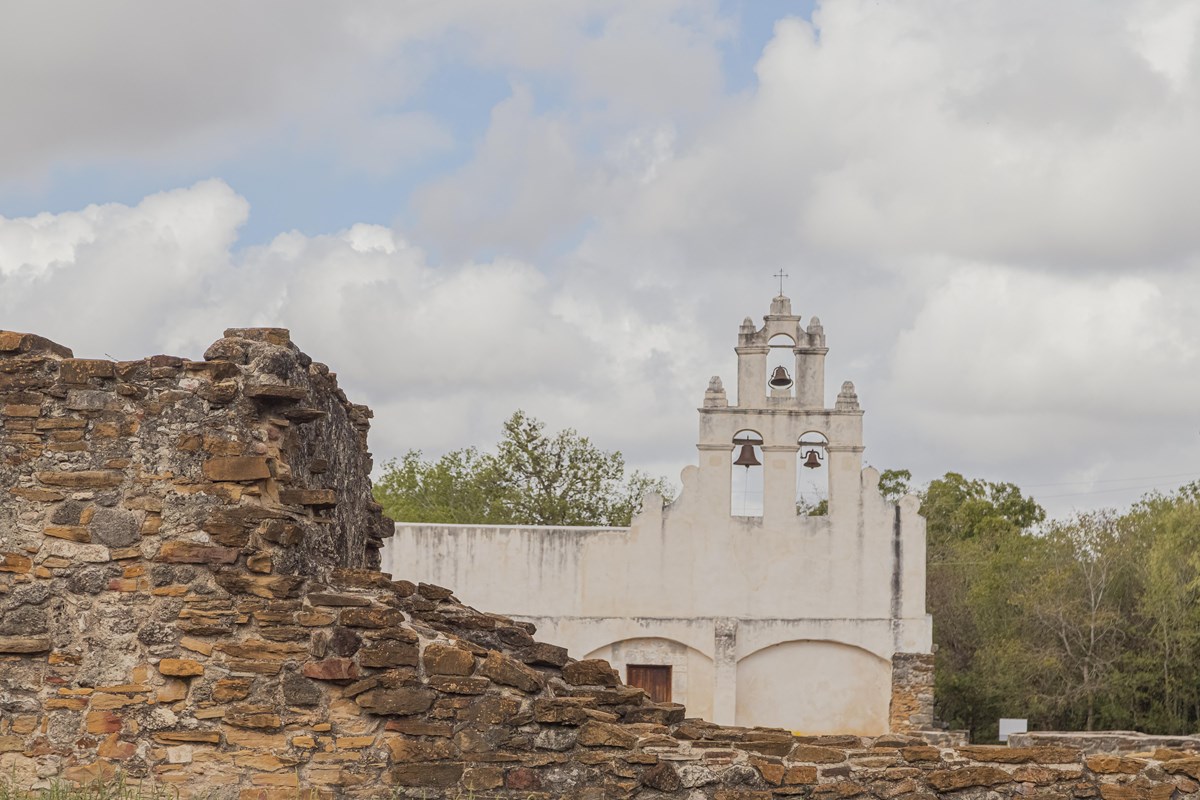 White frescoed church with a stone ruin to the left in the foreground. 