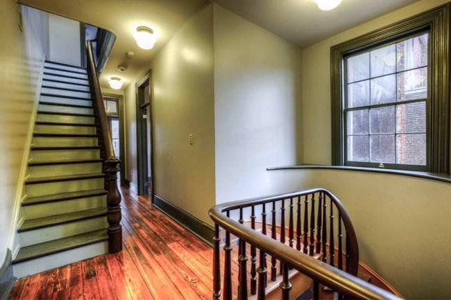 The second level in a historic home with wooden floorboards, steps, railings, light fixtures, window