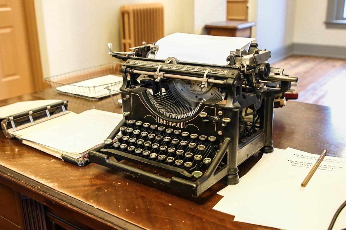 Old-fashioned type writers sits on top of a desk with other office supplies