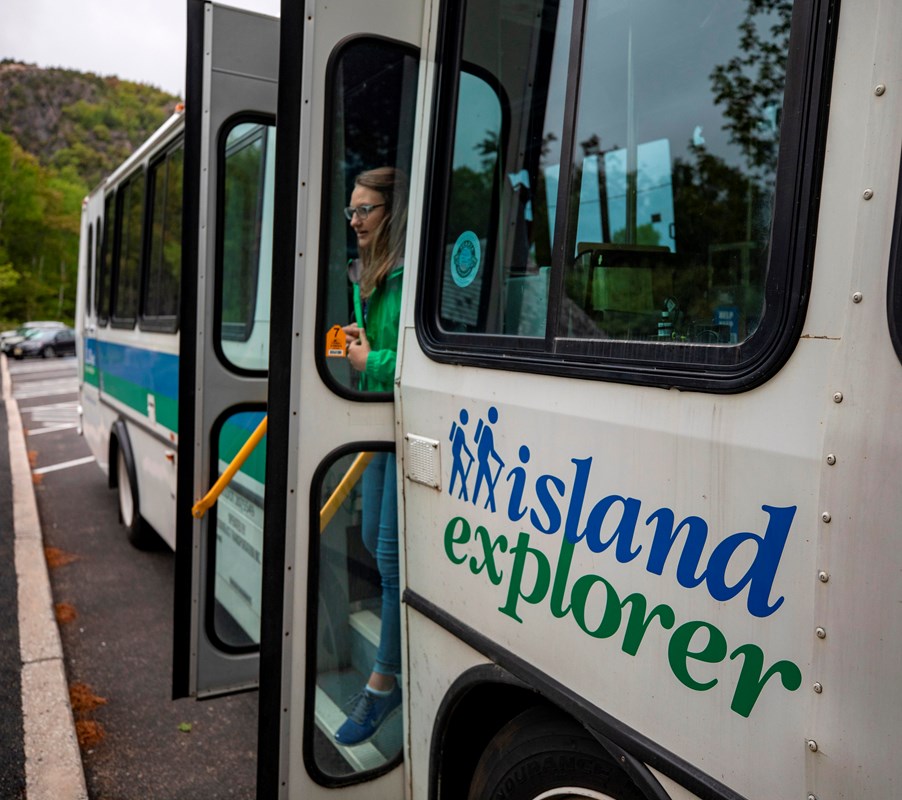 Woman steps out of the open double-doors of a white bus labeled Island Explorer.