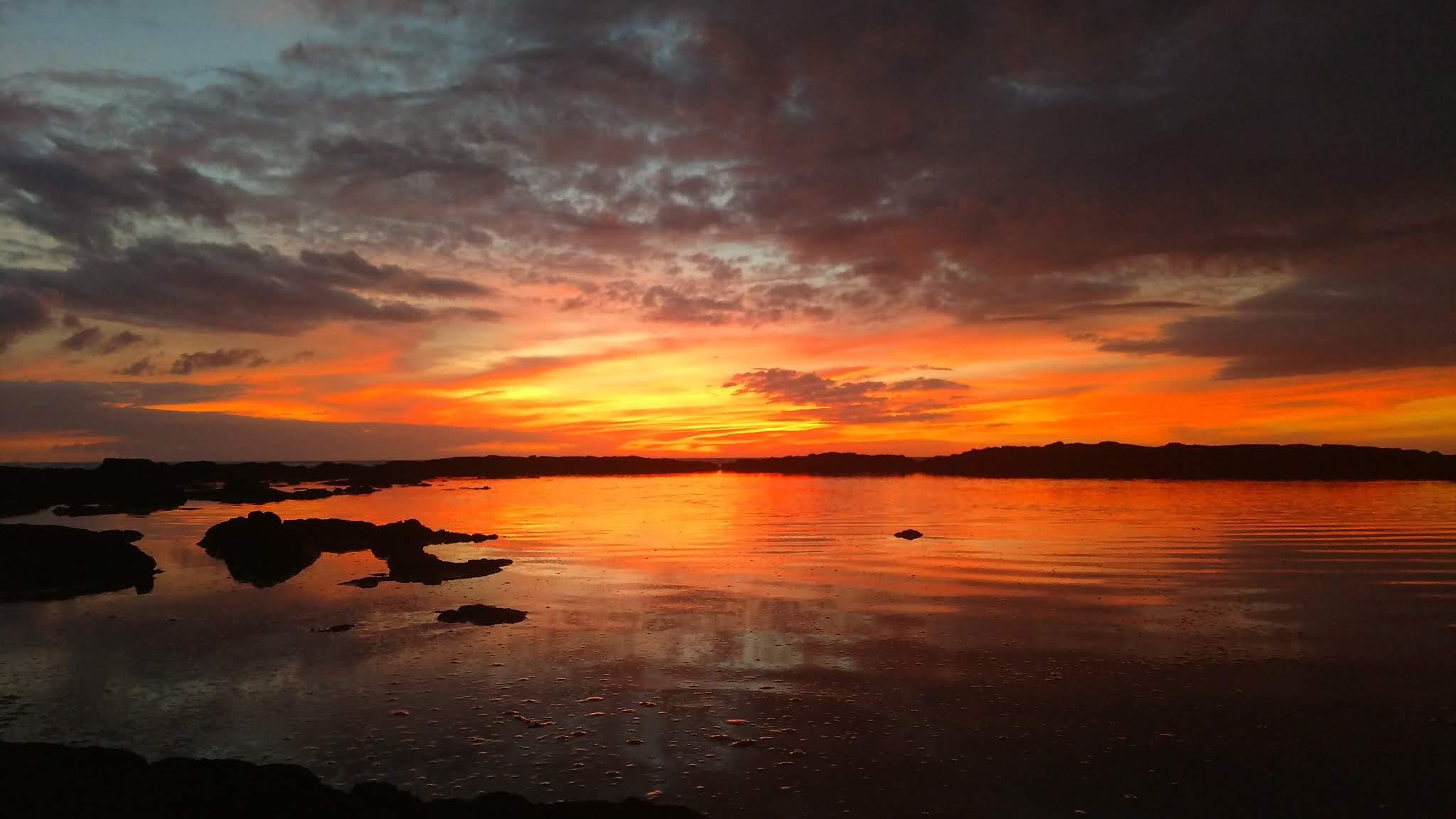 A glowing sunset reflects in the calm waters of a tide pool.