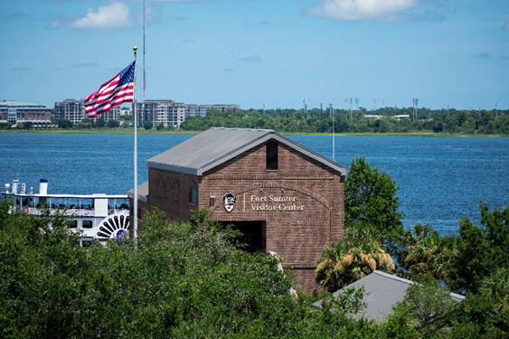 A three-story brick structure with a staircase in front and water in the background