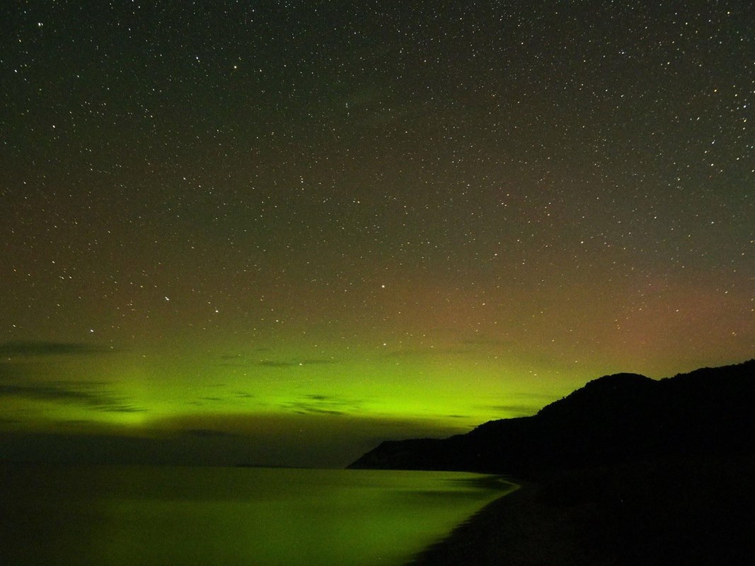 A glowing yellow and red northern light display with stars over a body of water