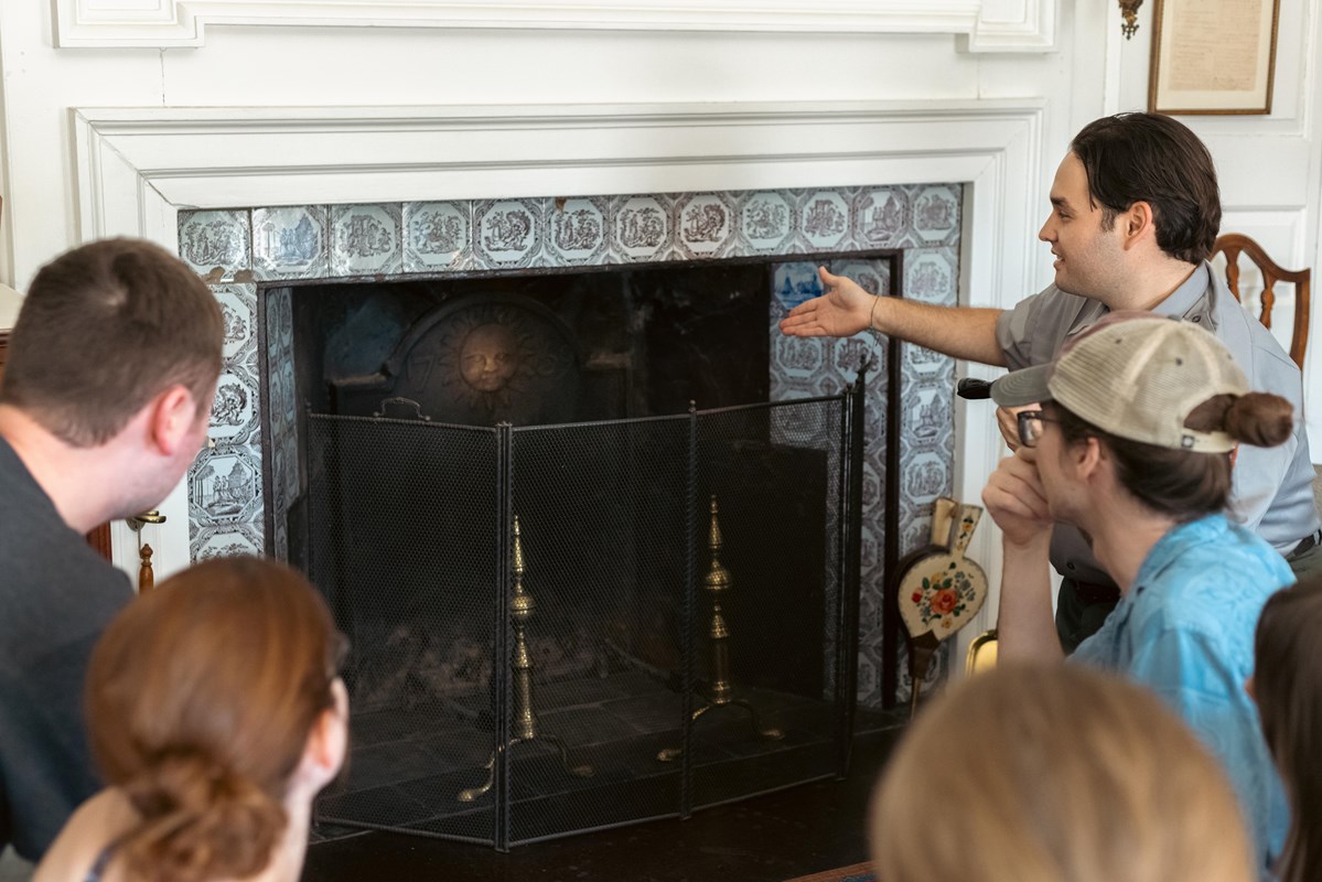Park ranger and visitors crouch in front of an 18th century fireplace