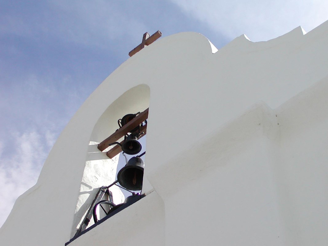 A cross and bell on the roof alcove of a white stucco church.