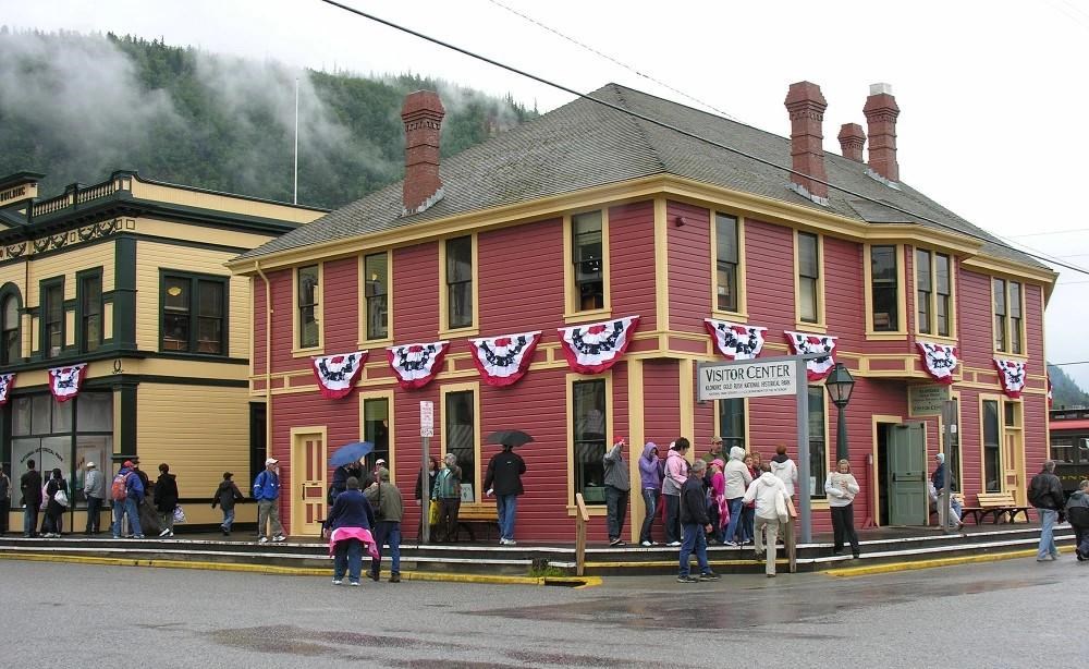 Visitors stand on a boardwalk outside a brick red colored wooden building with tidy golden trim.