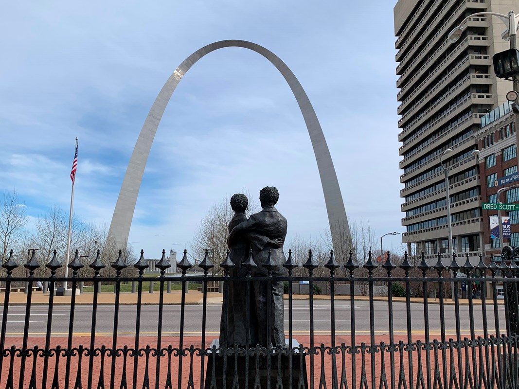 statue of a woman and man embracing in behind a black iron gate in front of the Arch 