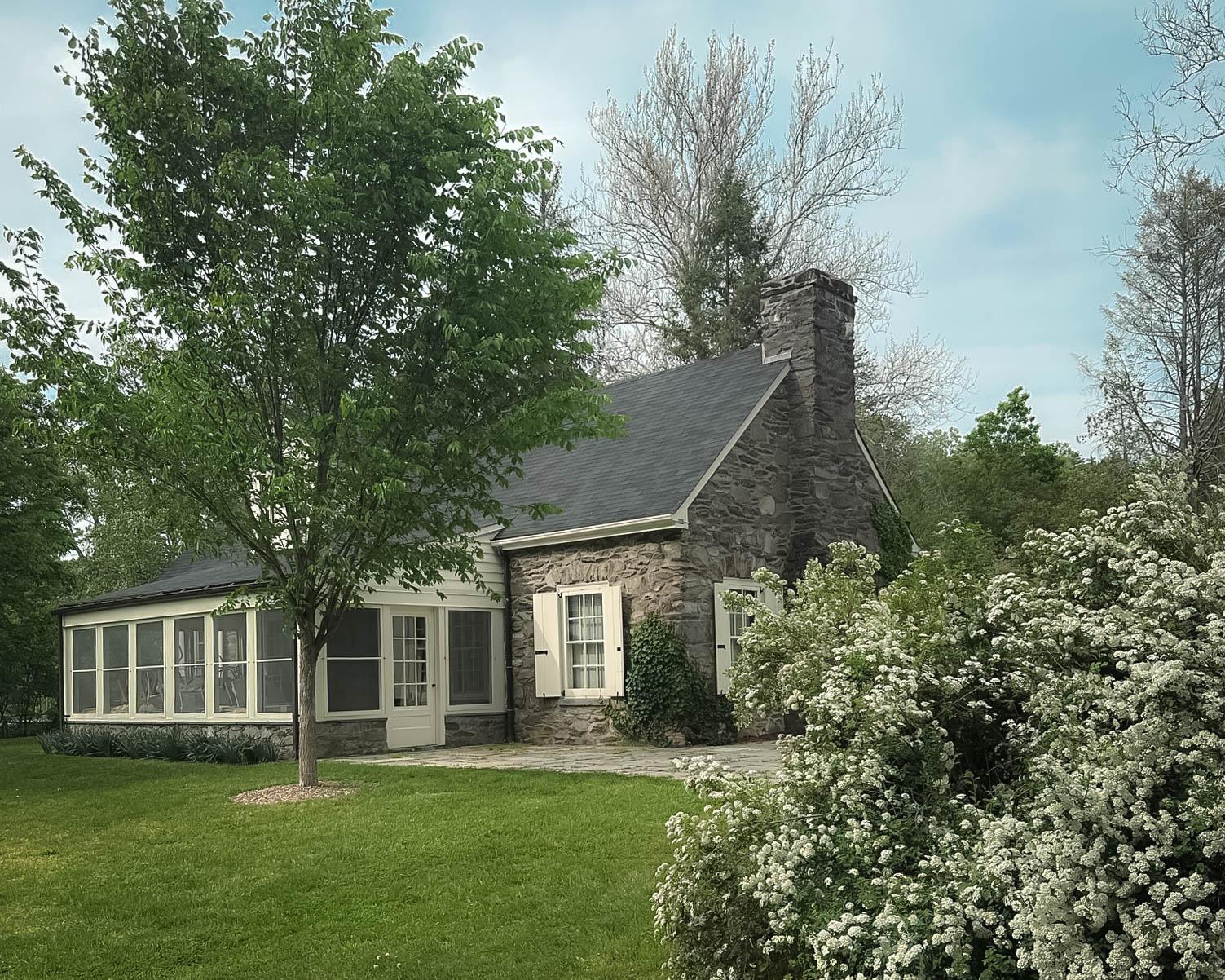 A small fieldstone cottage on a lush lawn with flowering shrubs.