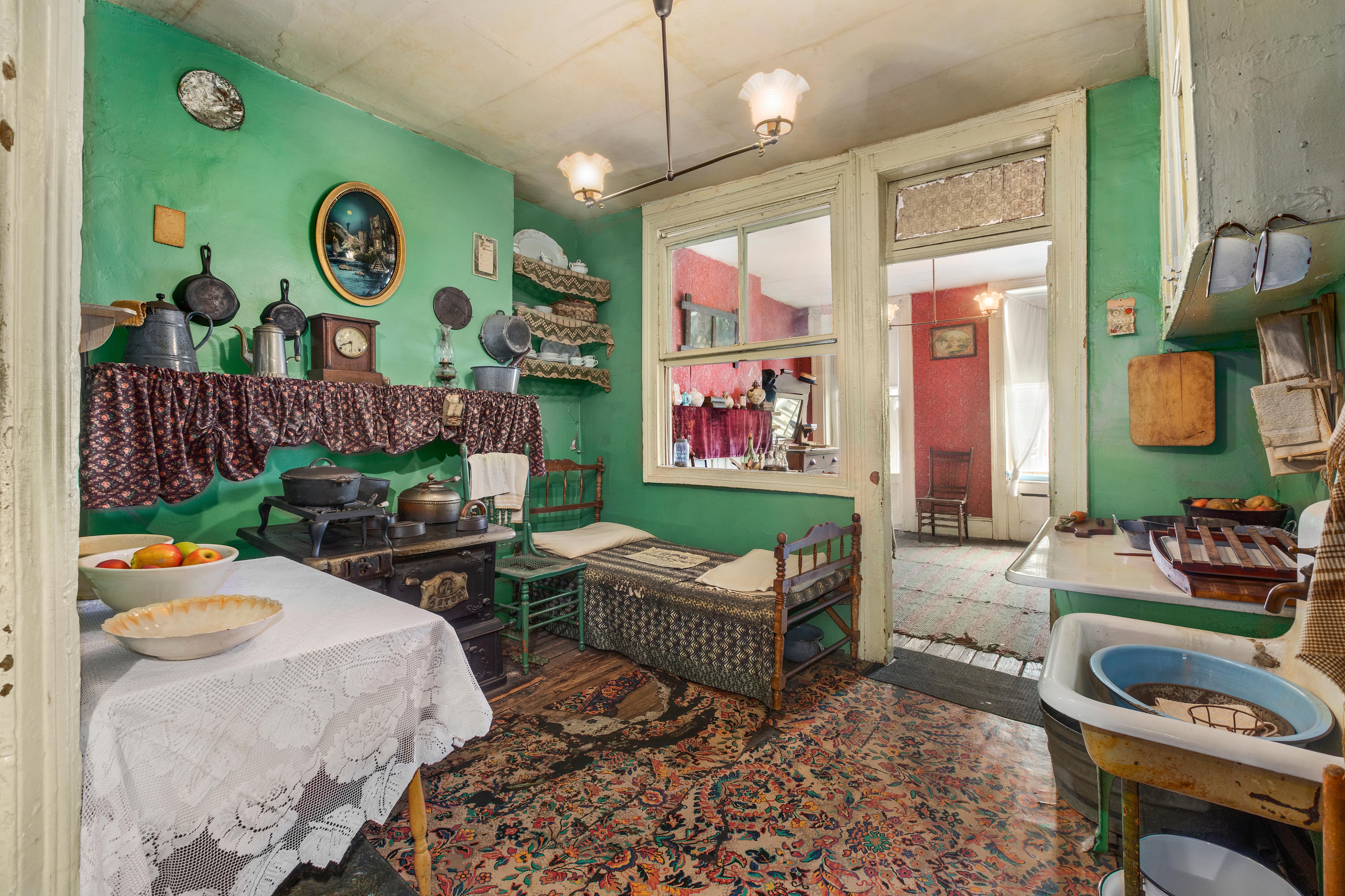 A tenement kitchen with cast iron posts, old stove, and a bed next to the stove