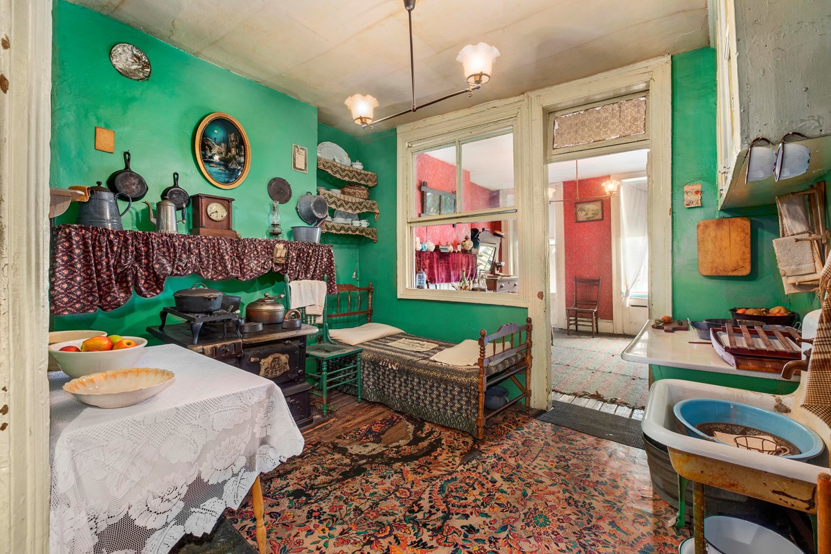 A tenement kitchen with cast iron posts, old stove, and a bed next to the stove