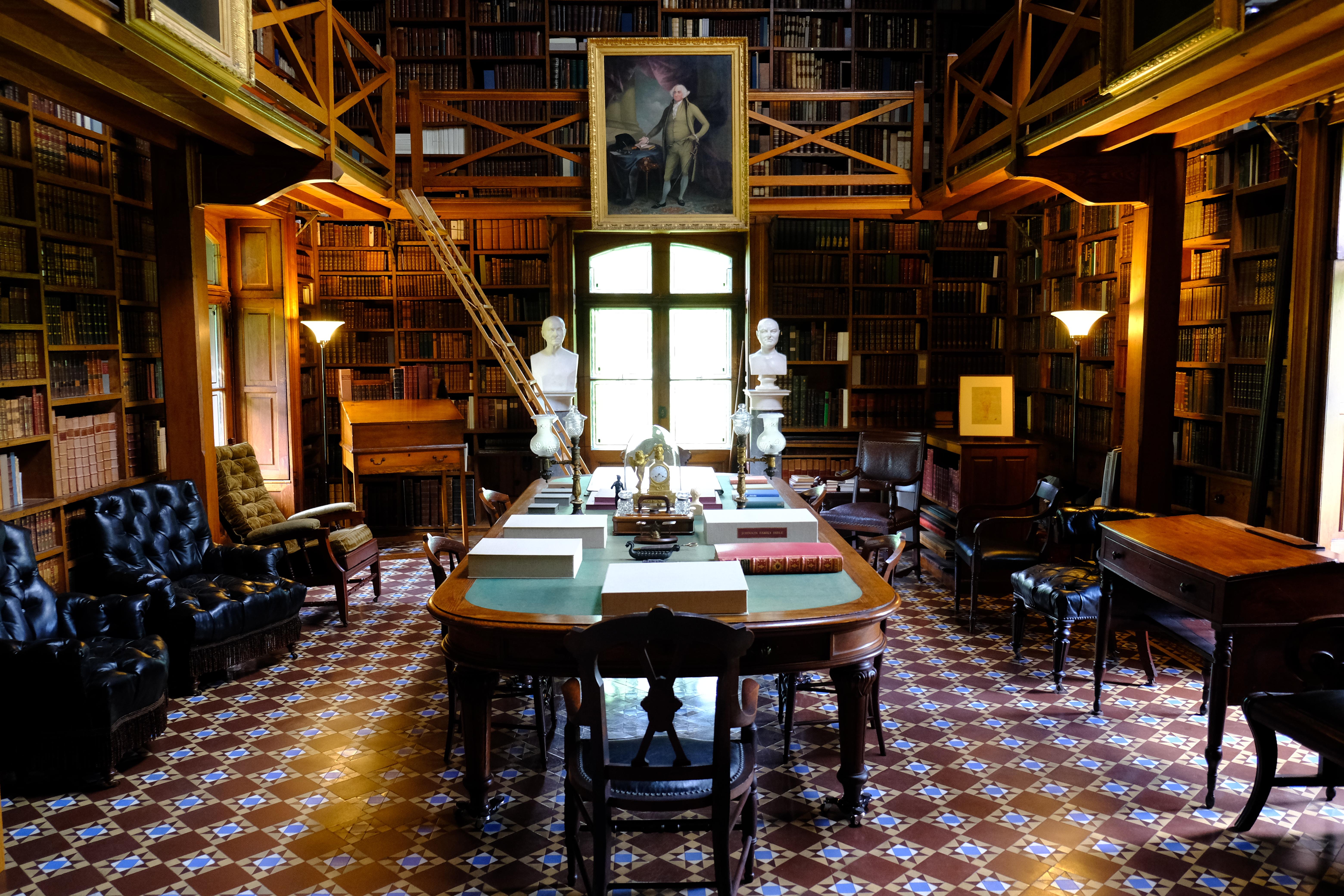 A dark room with tiled floor, filled with chairs and desks, with books lining the walls.