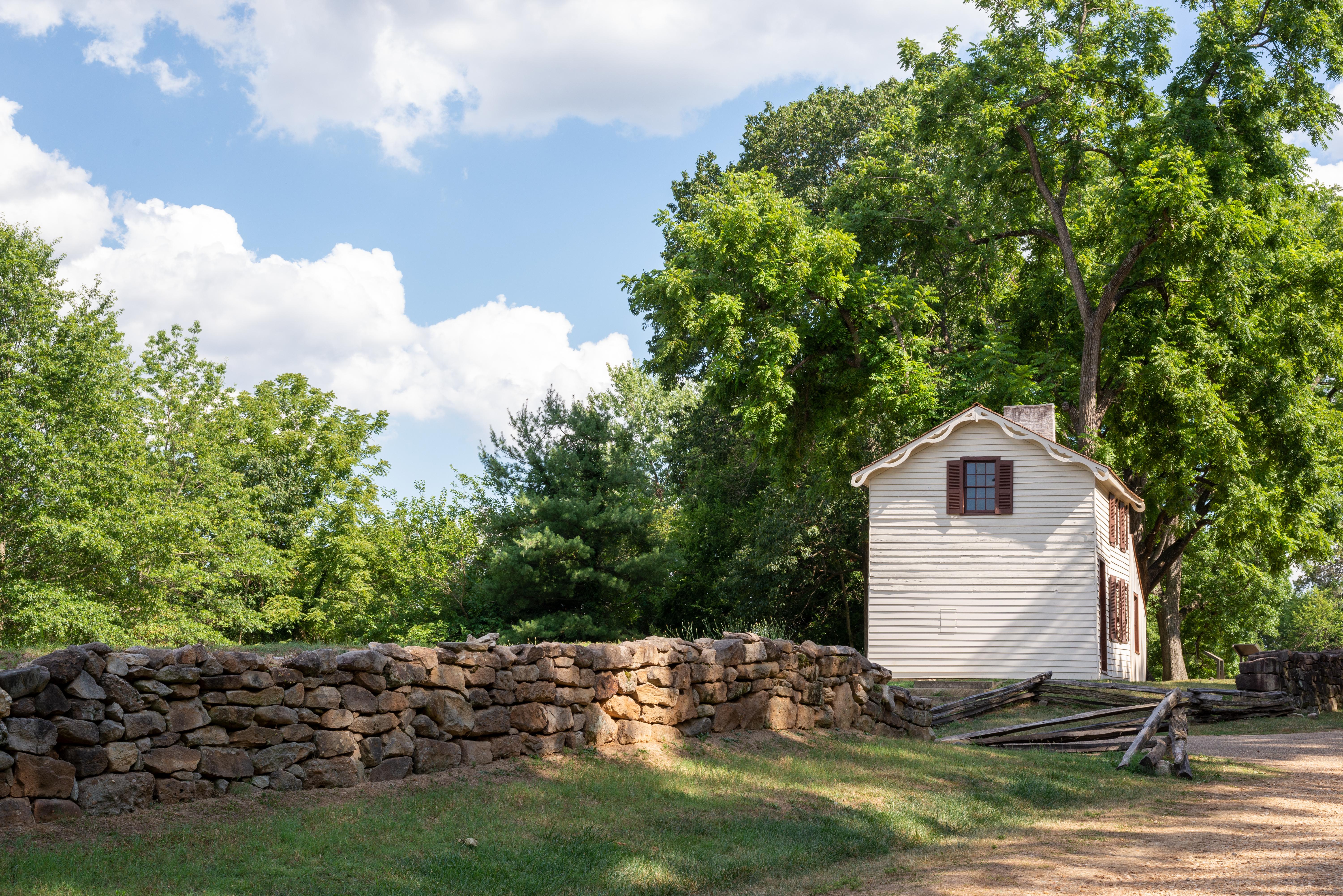 A gravel path bordered by a stone wall leading to a small, two story white house.