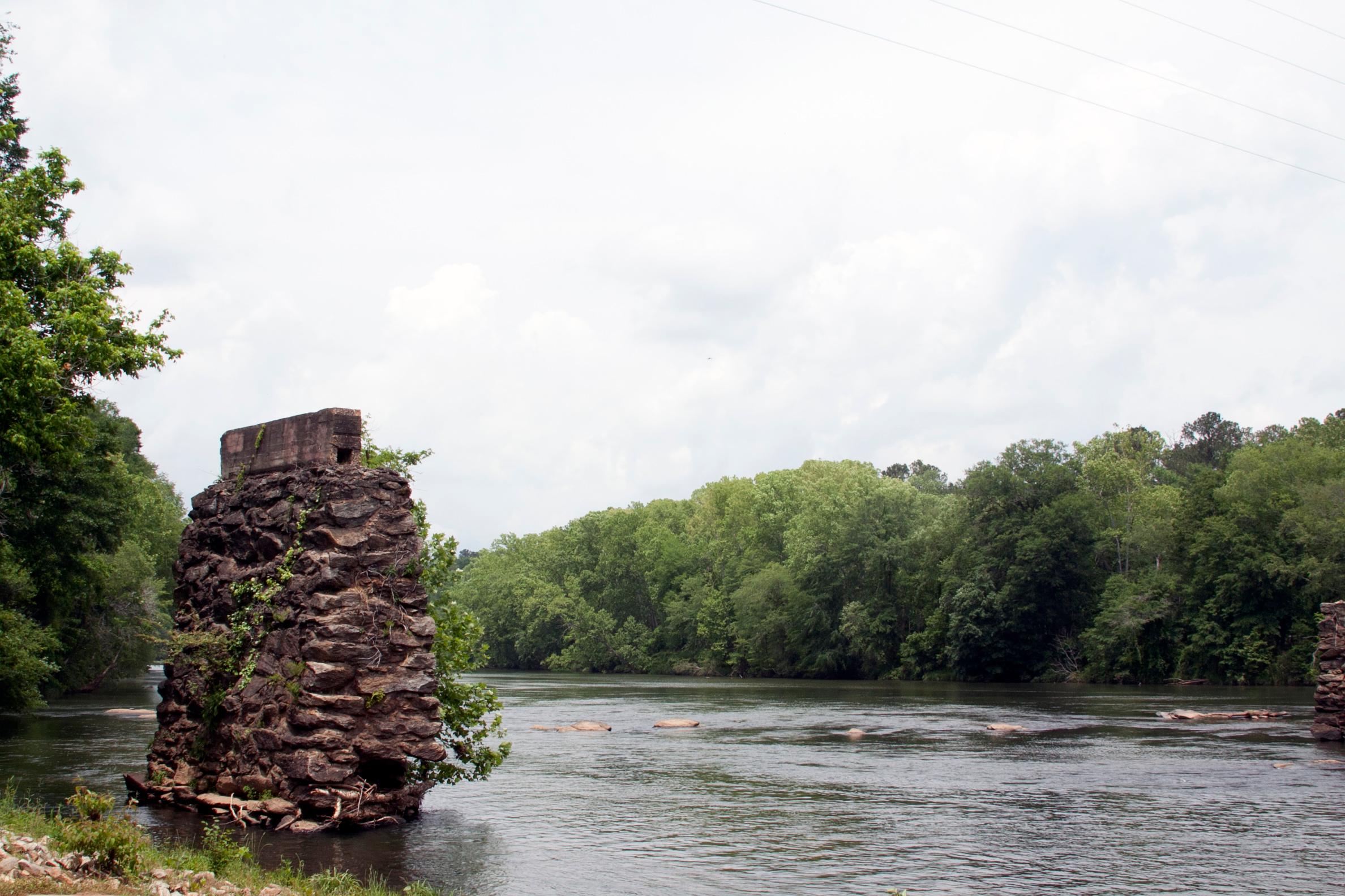 flat river, green trees lining banks, old bridge pier made of stones in river on left side of photo