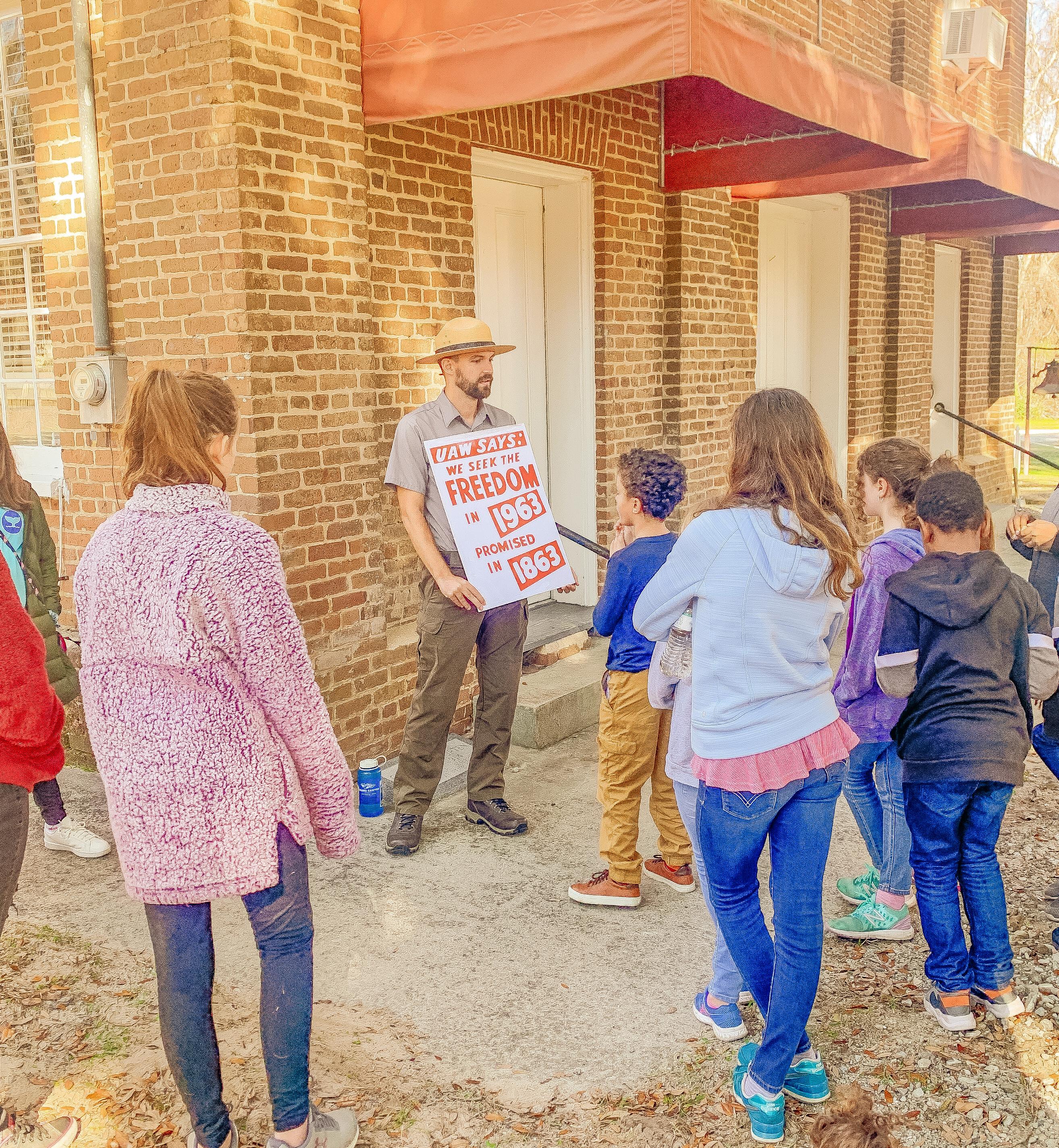 A park ranger holds a sign while talking to young people.