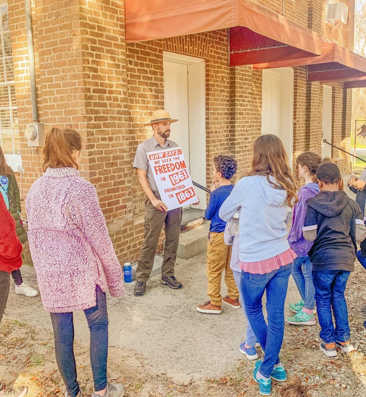 A park ranger holds a sign while talking to young people. 