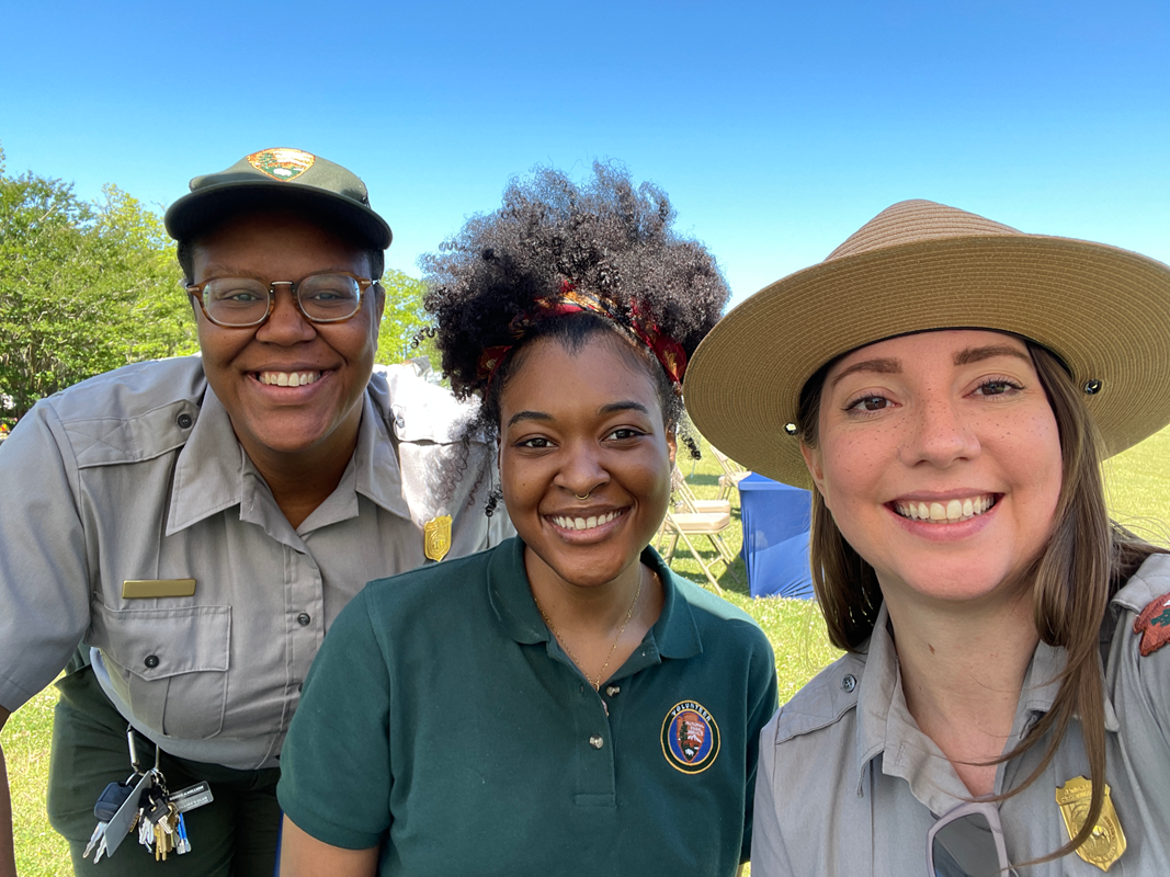 Three women, two in ranger uniforms, and one in a green polo smile at the camera.