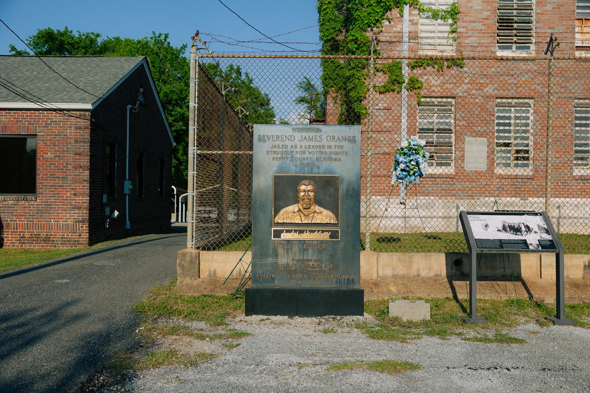A black granite looking monument in front of a dilapidated brick building.