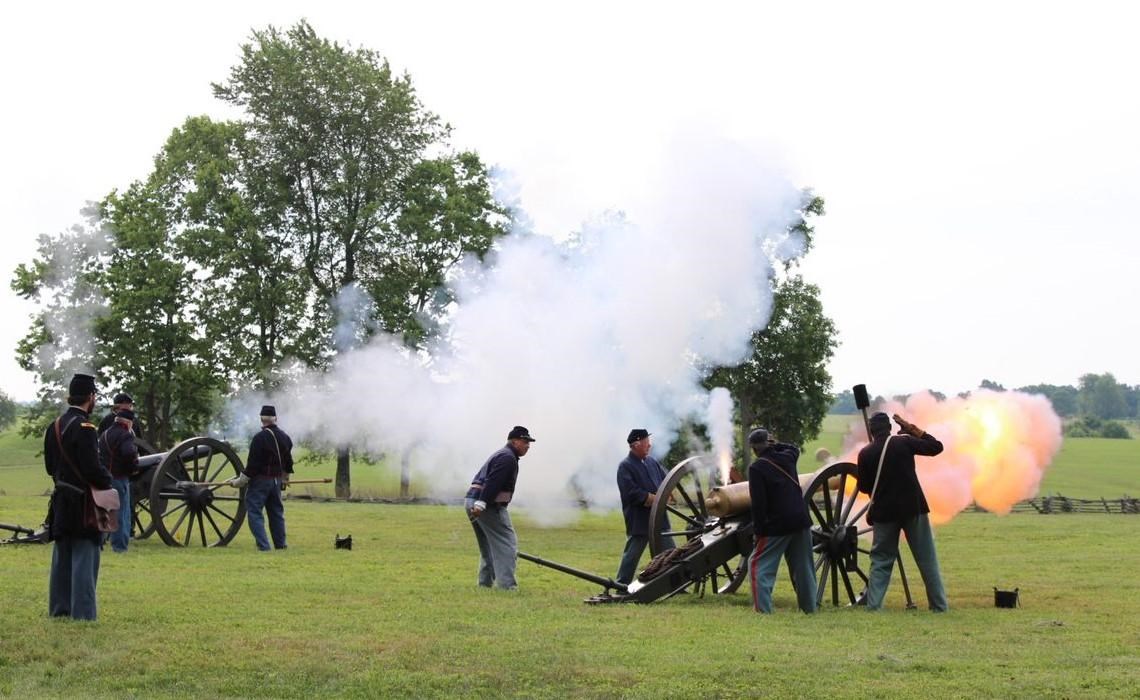 Living historians firing cannons in a grass field. 
