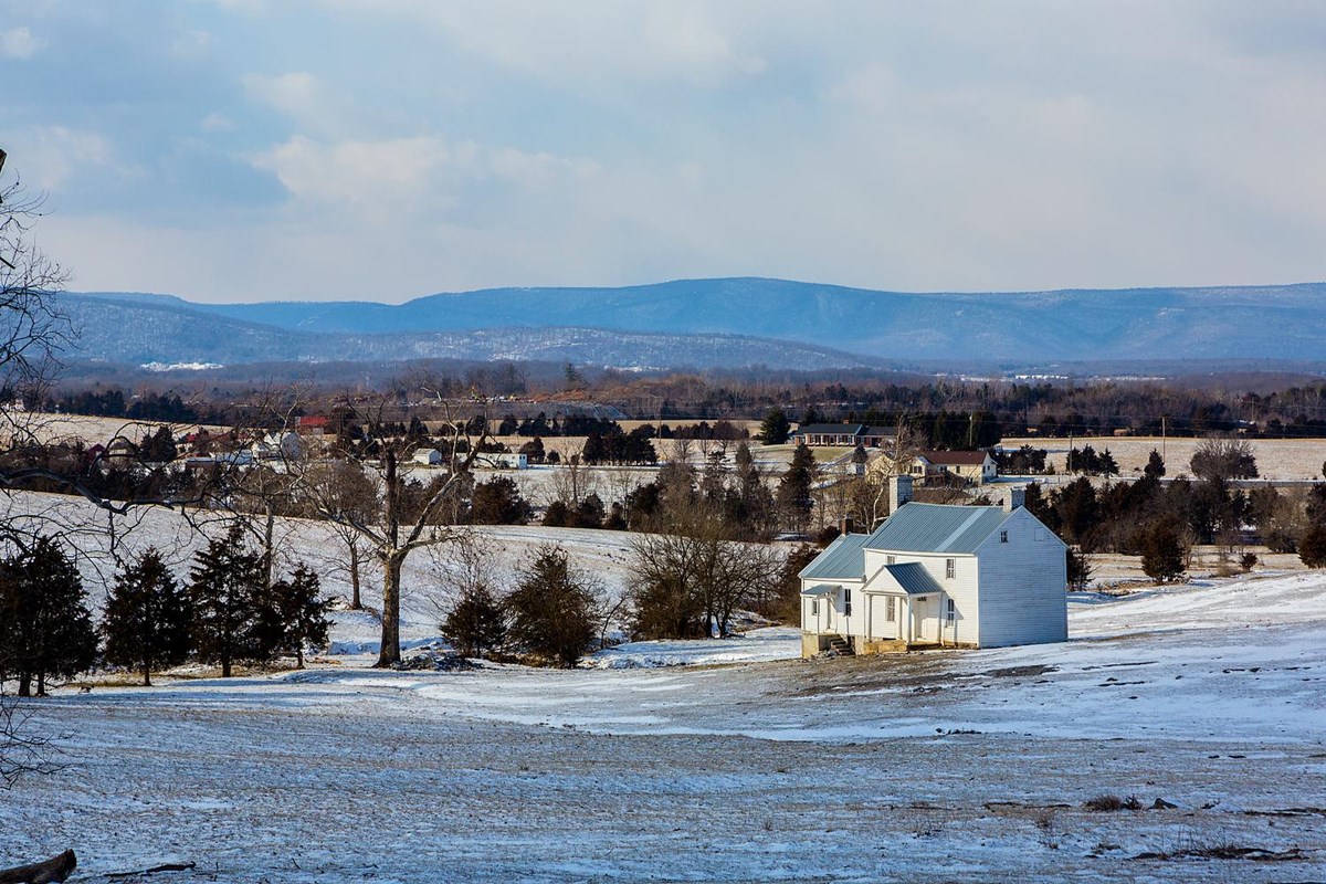 A white frame 1800s farmhouse stands alone in a snowy field. 