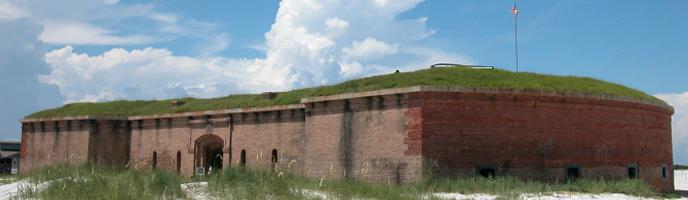 A brick fort stands on the edge of a white sand beach.