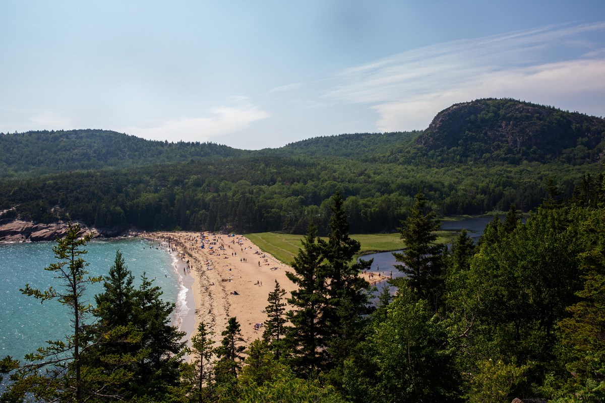 Landscape photo of a wide ocean cove with a sand beach with densely wooded mountains and ridges in t