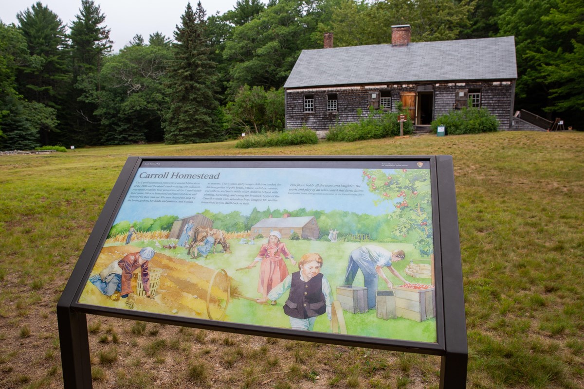 Landscape photo with a small historic farmhouse in the distance and an interpretive wayside in the f